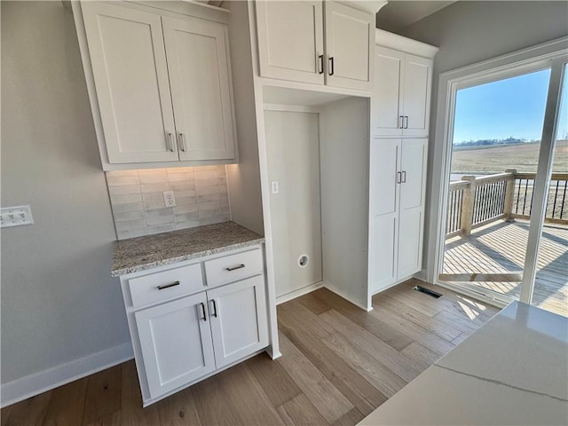 kitchen with white cabinets, light wood-type flooring, backsplash, and light stone countertops