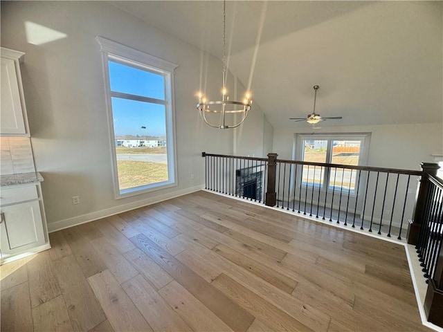 unfurnished dining area with ceiling fan with notable chandelier, light hardwood / wood-style floors, and vaulted ceiling