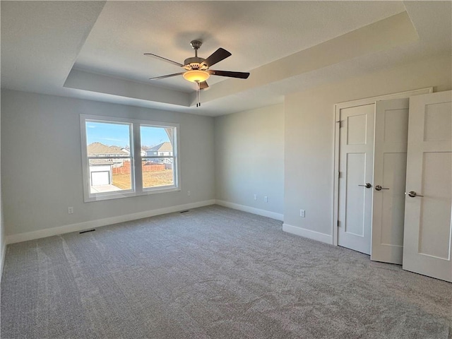 empty room featuring a tray ceiling, ceiling fan, and carpet floors