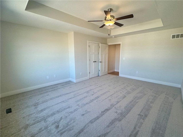 carpeted spare room featuring a raised ceiling and ceiling fan