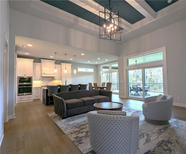 living room with beam ceiling, hardwood / wood-style flooring, a towering ceiling, and an inviting chandelier