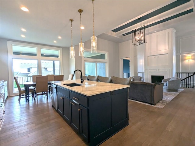 kitchen featuring light stone countertops, sink, hanging light fixtures, hardwood / wood-style flooring, and a center island with sink