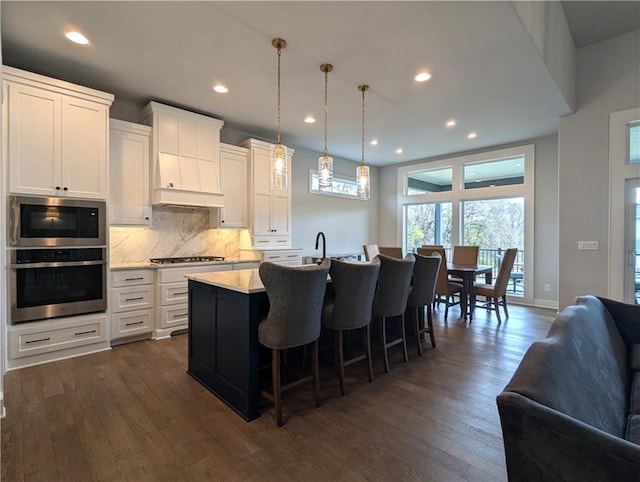 kitchen with a kitchen island with sink, decorative light fixtures, white cabinets, and dark hardwood / wood-style flooring