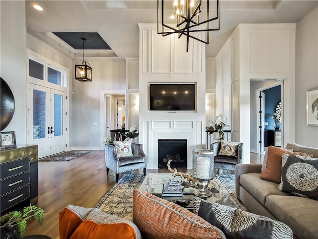 living room featuring a large fireplace, a raised ceiling, a chandelier, ornamental molding, and dark hardwood / wood-style floors