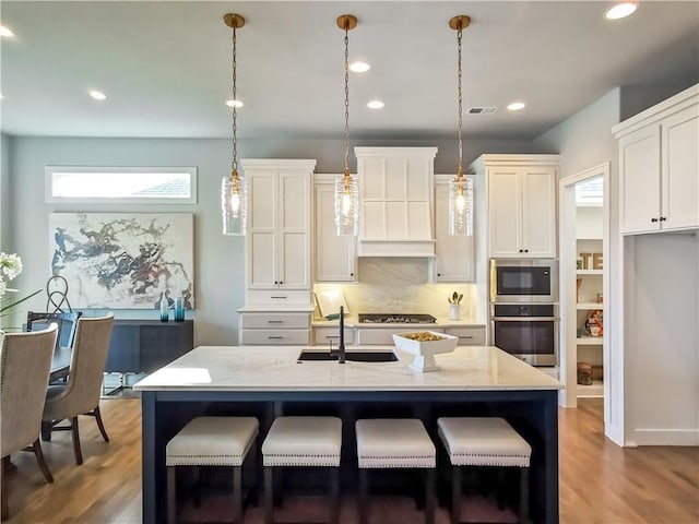 kitchen with appliances with stainless steel finishes, sink, pendant lighting, and an island with sink