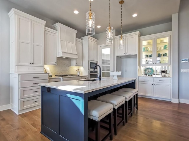 kitchen with white cabinetry, a kitchen island with sink, light wood-type flooring, decorative light fixtures, and stainless steel appliances