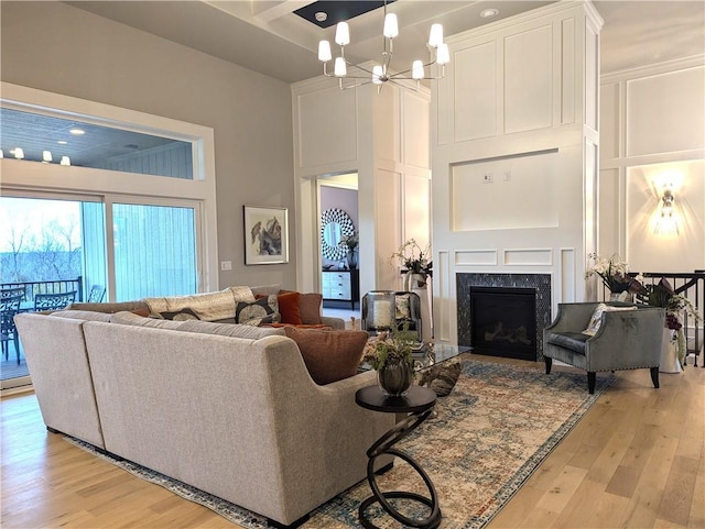 living room featuring a fireplace, a towering ceiling, light hardwood / wood-style floors, and a chandelier