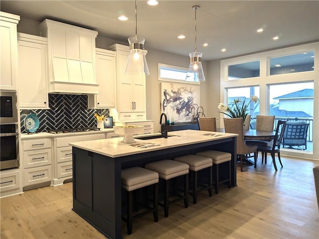 kitchen featuring decorative backsplash, appliances with stainless steel finishes, a center island with sink, white cabinets, and hanging light fixtures