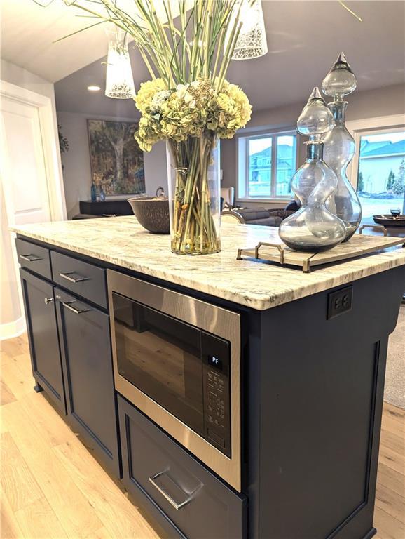 kitchen with built in microwave, light hardwood / wood-style flooring, a kitchen island, and light stone counters