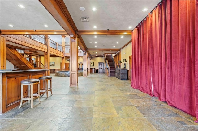 interior space featuring bar, decorative columns, ornamental molding, and tile flooring