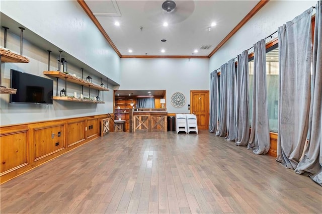 interior space featuring a towering ceiling, ornamental molding, and light hardwood / wood-style floors