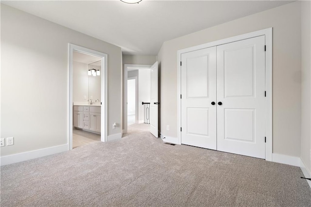 unfurnished bedroom with light carpet, a closet, sink, and ensuite bathroom