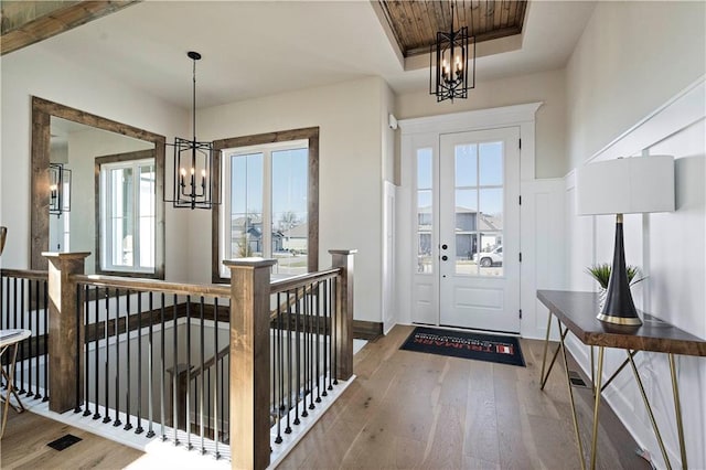 foyer entrance with an inviting chandelier, a wealth of natural light, hardwood / wood-style flooring, and a raised ceiling