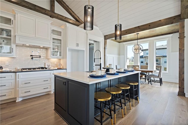 kitchen with white cabinetry, vaulted ceiling with beams, a kitchen breakfast bar, light hardwood / wood-style floors, and a center island with sink