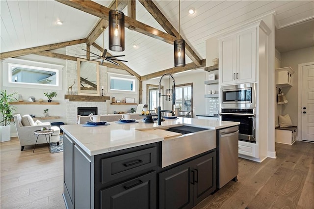 kitchen featuring stainless steel appliances, wood-type flooring, beam ceiling, white cabinetry, and a stone fireplace