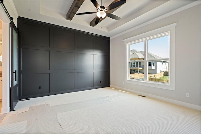 carpeted spare room with ceiling fan, a wealth of natural light, a barn door, and a tray ceiling