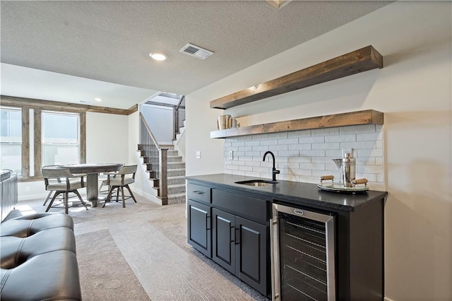 bar featuring backsplash, sink, beverage cooler, light carpet, and a textured ceiling