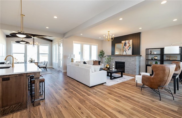 living room with wood-type flooring, sink, a fireplace, beamed ceiling, and a chandelier