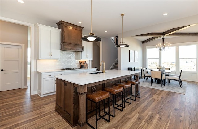 kitchen with dark wood-type flooring, white cabinets, pendant lighting, and an island with sink