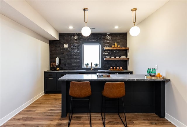 bar featuring sink, light hardwood / wood-style floors, pendant lighting, dark stone countertops, and brick wall