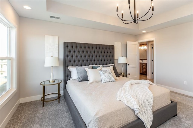 carpeted bedroom with ensuite bathroom, a tray ceiling, and a chandelier