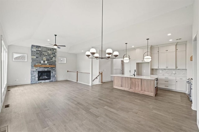 kitchen with white cabinets, a stone fireplace, hanging light fixtures, lofted ceiling, and an island with sink