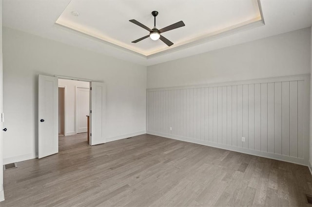 empty room with a raised ceiling, ceiling fan, and hardwood / wood-style floors