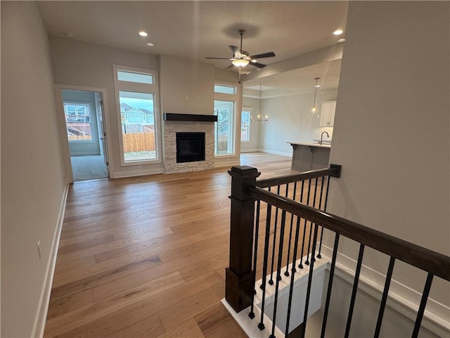 interior space featuring ceiling fan with notable chandelier, light hardwood / wood-style floors, a stone fireplace, and sink