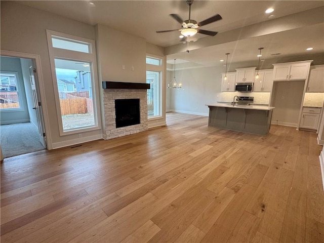 unfurnished living room with a fireplace, light hardwood / wood-style floors, and ceiling fan with notable chandelier