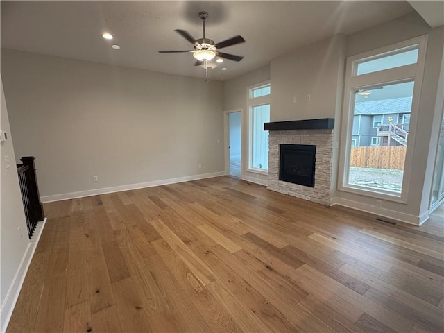 unfurnished living room with a stone fireplace, ceiling fan, and light hardwood / wood-style flooring