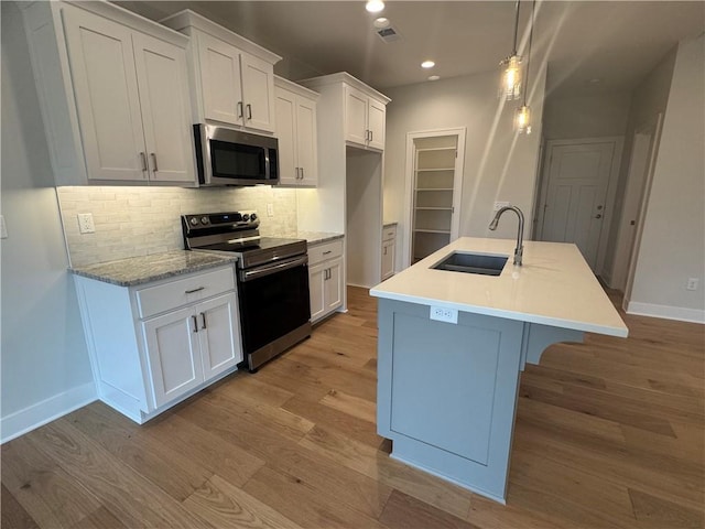 kitchen with white cabinetry, a center island with sink, stainless steel appliances, and light wood-type flooring