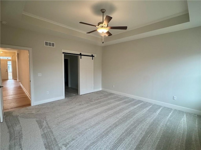 unfurnished bedroom featuring a raised ceiling, a barn door, ceiling fan, and light carpet