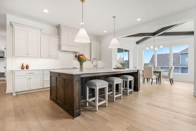 16743 S Hall St, Olathe, KS 66062 - kitchen with custom exhaust hood, light wood-style flooring, light countertops, a kitchen island with sink, and a sink