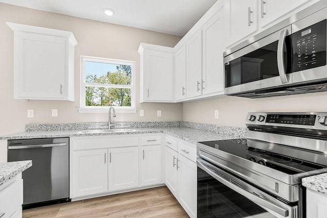 kitchen with light stone counters, white cabinetry, stainless steel appliances, and a sink