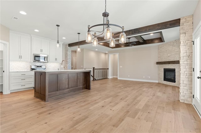 kitchen featuring a center island with sink, light hardwood / wood-style floors, white cabinets, beamed ceiling, and pendant lighting