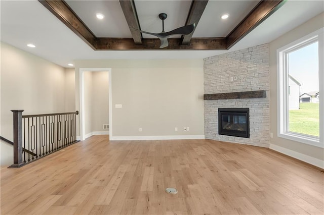 unfurnished living room featuring beam ceiling, light wood-type flooring, and a stone fireplace