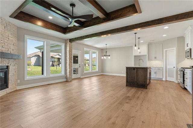 unfurnished living room featuring sink, ceiling fan with notable chandelier, light wood-type flooring, and a fireplace