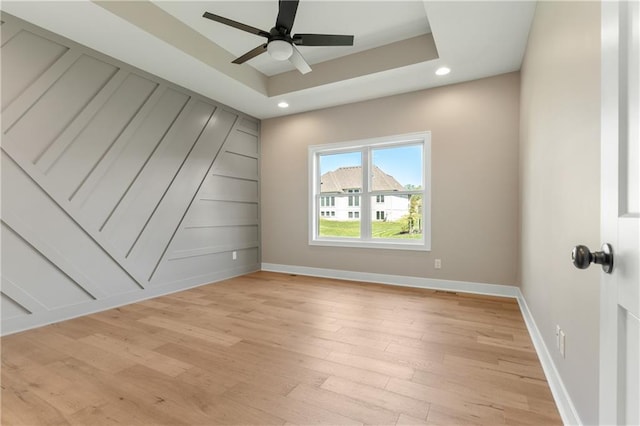 empty room with ceiling fan, a tray ceiling, and light wood-type flooring