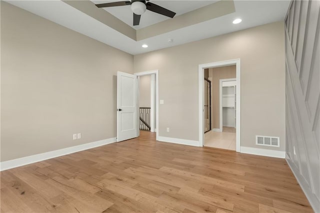 unfurnished bedroom featuring a spacious closet, light hardwood / wood-style flooring, ceiling fan, and a tray ceiling