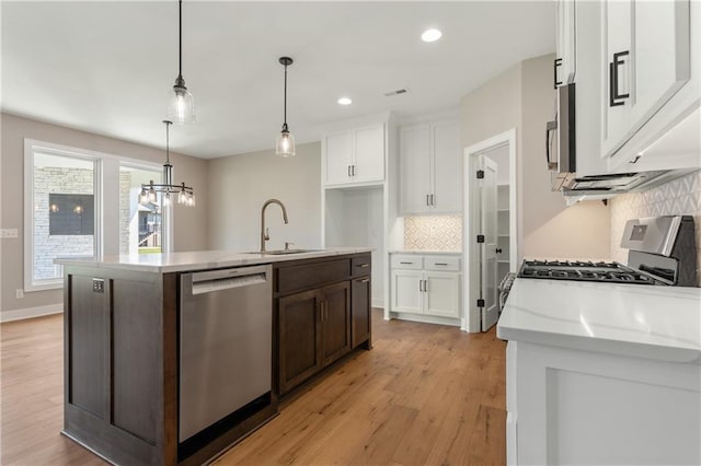 kitchen with light wood-type flooring, backsplash, stainless steel appliances, sink, and an island with sink