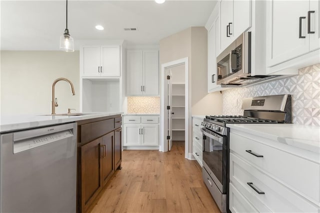 kitchen with decorative light fixtures, backsplash, light hardwood / wood-style flooring, stainless steel appliances, and white cabinetry