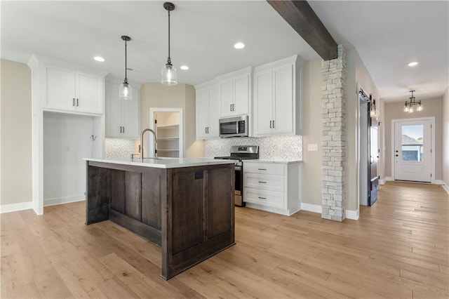 kitchen featuring backsplash, light wood-type flooring, stainless steel appliances, a center island with sink, and pendant lighting