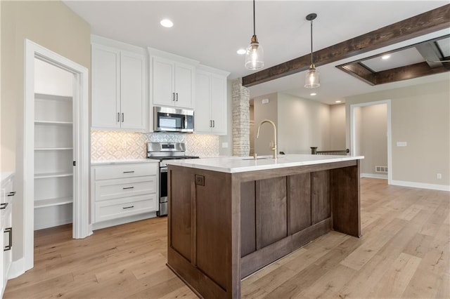 kitchen featuring a kitchen island with sink, beamed ceiling, light hardwood / wood-style flooring, appliances with stainless steel finishes, and tasteful backsplash