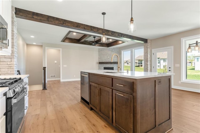 kitchen with decorative light fixtures, stainless steel appliances, an island with sink, beamed ceiling, and light wood-type flooring