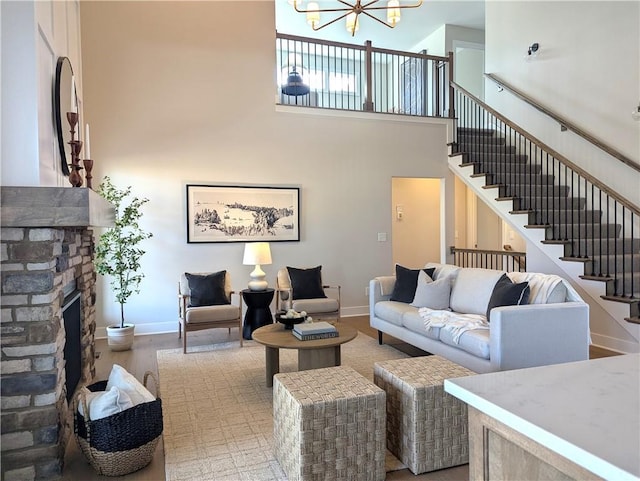 living room featuring an inviting chandelier, a towering ceiling, a stone fireplace, and light hardwood / wood-style flooring