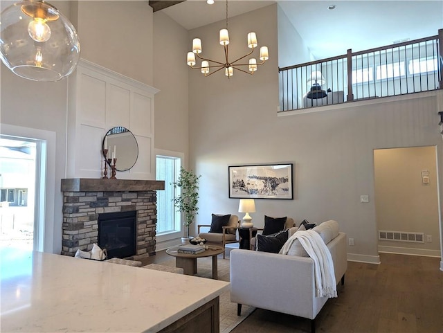 living room with a stone fireplace, a towering ceiling, a notable chandelier, and dark hardwood / wood-style floors