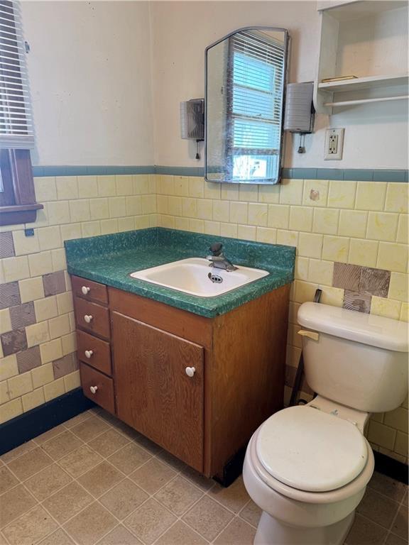 half bathroom with vanity, a wainscoted wall, tile walls, toilet, and tile patterned floors