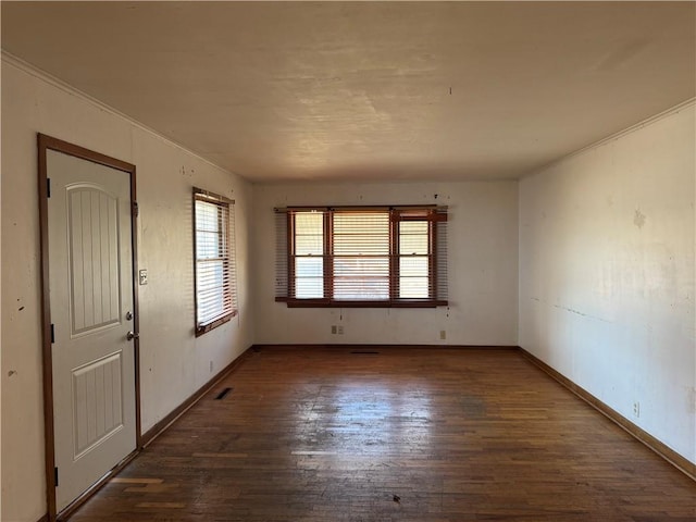 empty room featuring dark wood-style floors, visible vents, a wealth of natural light, and baseboards