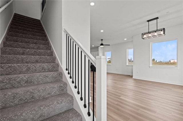 staircase with ceiling fan with notable chandelier and hardwood / wood-style flooring