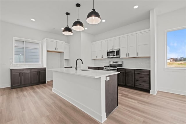 kitchen with stainless steel appliances, light hardwood / wood-style floors, sink, white cabinets, and pendant lighting